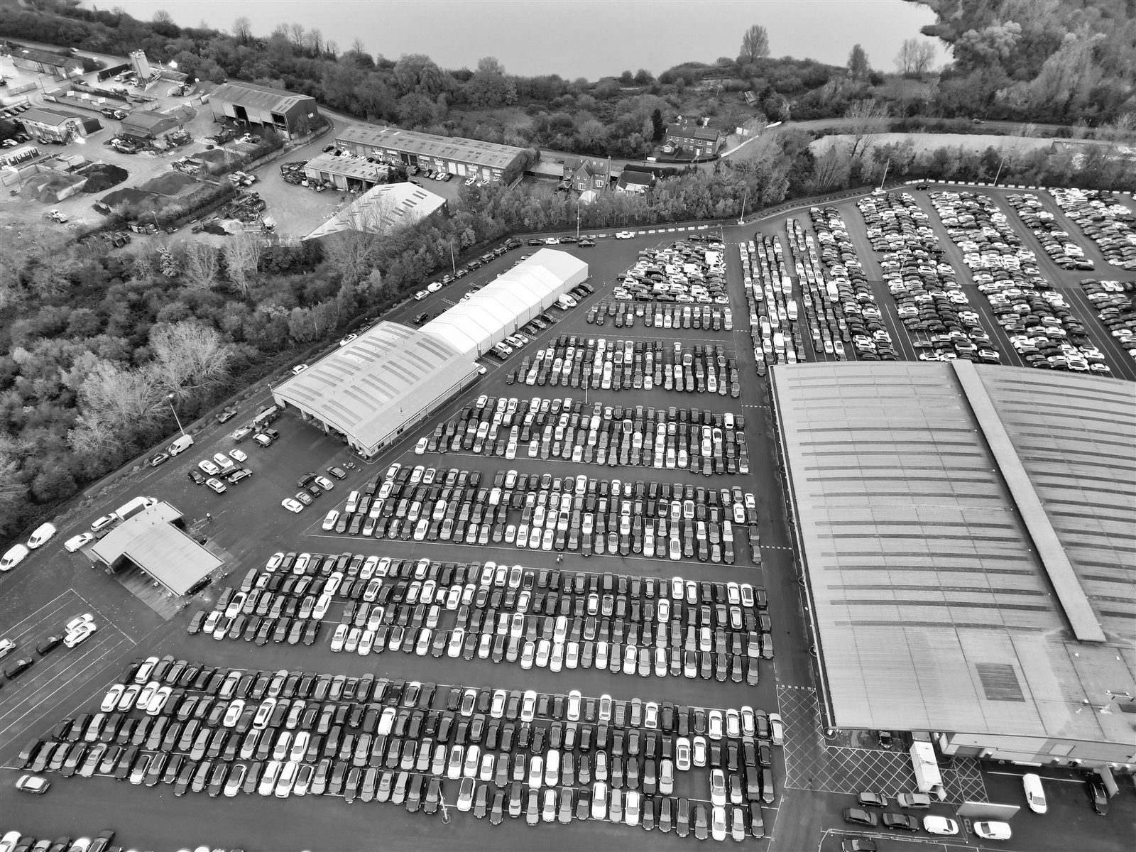 Vista aerea di un grande piazzale con centinaia di automobili parcheggiate all'aperto, esposte alla grandine